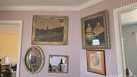 Wall with five framed items: watercolor painting, photograph of two girls, oval mirror, small photograph, and a pencil drawing with pink matte.