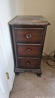 Front view of the antique Kindel nightstand showing three drawers with round wooden knobs and overall worn finish.