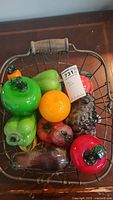 Photo showing top view of wire basket with variety of blown glass fruit and vegetables inside, colorful and detailed glass pieces visible.