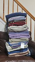 Photo showing a stack of assorted bath towels including navy blue, red, cream, lavender, and gray colors on a chair by staircase
