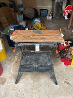 Front view of Black and Decker Workmate 400 foldable worktable showing wooden slatted top with damage, orange adjustment knobs, black metal legs and frame, and lower footrest detailing.