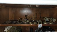 Shelf displaying brass candlesticks, bookends, cast iron trivet, fly ashtray, and grasshopper figurine.