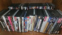 Photo showing two rows of assorted DVDs on shelves, with variety of movie titles and genres visible.