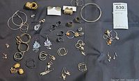 Top-down view of assorted earrings laid on black cloth showing variety of types and materials including gold and silver tones, some with gemstones.
