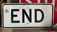 Metal traffic sign sized about 15x30 inches with 'END' printed in black on white reflective surface with black border. Shows scratches and dirt.