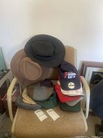 Photo showing a variety of men's hats including a gray felt bucket hat, brown bucket hat, several baseball caps including a navy blue Philadelphia Phillies cap, red and white plaid cap, and green cap.