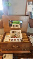 Wooden jewelry box closed with a white plastic basket on top containing assorted pins, charms, and jewelry parts. The box measures approximately 12.5 x 8.5 x 6 inches.