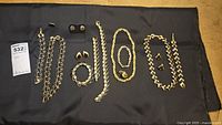 Full view of gold tone and black enamel bracelets, necklaces, and earrings laid out on black fabric, showing clasp damage and enamel condition.