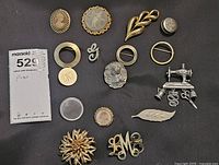 All 16 pins arranged on flat surface showing variety including Monet flower and Danecraft sewing machine