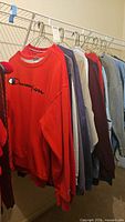 Photo showing hanging sweatshirts and henleys on wire shelf rack, various colors from red, grey, blue, maroon, navy