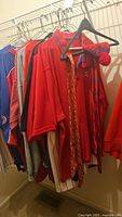 Image showing assorted sports apparel including red Phillies jerseys and shirts hanging in a closet.