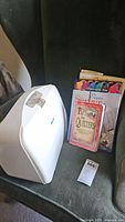 White Baby Lock Pro Quilt Model BL2600 quilting machine with handle next to a stack of quilting/sewing books on a dark green chair.