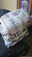 Stack of folded quilts displayed on a chair showing patchwork and floral design details