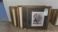 Nine framed flower prints by Robert Furber arranged leaning together on floor and carpet, showcasing various frame styles and mat colors for the floral prints.