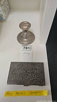 Photo showing weighted sterling silver candlestick and intricately engraved 800 silver cigarette case by Jondell with auction tag