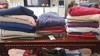 Folded stacks of various colored sweatshirts on a wooden table showing the quantity and colors including navy, beige, red, gray, and purples.