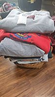 Stack of folded sweatshirts including a grey Temple University, red Mickey Mouse Disney, and grey item on the bottom.
