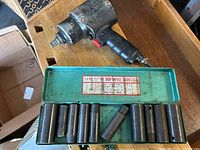 Photo of pneumatic impact wrench resting on green metal socket case with 12 deep impact sockets visible inside.