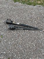 Two black metal fence spikes laid on gravel ground showing full length and mounting brackets.