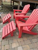 Two red Adirondack chairs with footstools on brick patio at an angle
