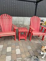 Two red Adirondack chairs and red side table positioned on patio pavers