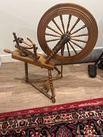 Full view of the antique wooden spinning wheel showing the wheel, base, and treadle on a wood floor.
