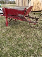 Side angle view of antique red wooden wheelbarrow with large metal spoked wheel, showing weathered paint and structure.