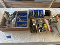 Full view of various boxes containing assorted hardware including locks, bolts, screws, hooks, keys, and other components laid out on a table.
