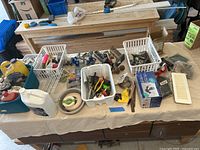 Assorted hand tools, hardware items, plastic baskets with screws and bolts, measuring tape, and various tools on a workshop table.