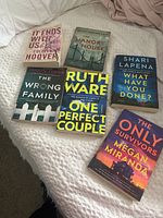 Photo showing six paperback books on a bed with titles and authors visible.