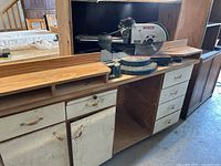 Overall view of Bosch miter saw mounted on custom wooden stand with drawers and cabinet.