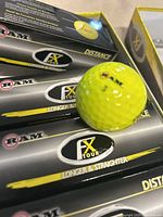 Close-up photo of yellow RAM FX Tour golf balls showing packaging and branding details such as 'longer and straighter' and 'distance'.