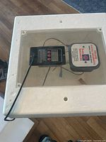 Top view of white insulated incubator box with digital control panel and automatic egg turner under clear lid.