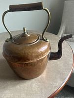 Side view of the vintage copper kettle showing the rounded body, wooden grip handle, and spout with patina.