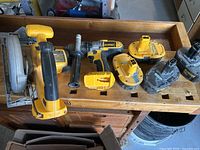 Dewalt cordless hammer drill with auxiliary handle, four 18V batteries, and circular saw on wooden surface