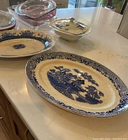 Overview of antique ceramic dishes with blue and white oriental motifs and several glass baking dishes on a kitchen counter.