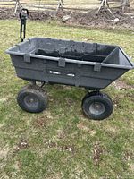 Side profile view of black dumping cart with plastic bed and pneumatic tires