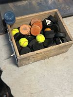 Wooden crate filled with assortment of hockey pucks and training pucks, showing multiple types and colors.