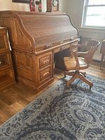 Front angled view of oak roll-top desk with chair in room