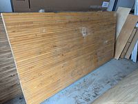 Full view of the maple bowling lane board leaning against the wall, showing the wood strips and surface condition.
