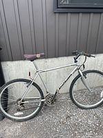 Side view of the silver Apollo 15-speed men's bike, showing whole frame, tires, seat and pedals.