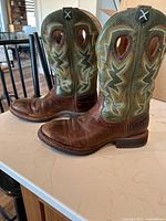Side view of the leather cowboy boots showing the brown foot with green shafts decorated with colorful stitching and cutout details.