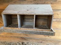 Front view of wooden nesting box showing three separate compartments and front perch designed for hens.