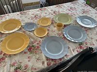 Full view of 9 vintage Grindley petalware pieces of pastel yellow and blue plates and a cup displayed on floral tablecloth.