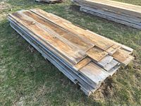 Stack of rough sawn pine boards on wooden pallets on grass, top surfaces visible
