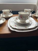 Front angle view of stacked cup, saucer, salad plate, and dinner plate showing floral Petit Point design and gold scalloped rim