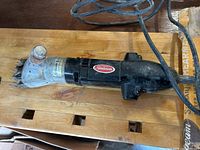 Electric sheep shears with black plastic body and metallic clipping head showing wear and a power cord.