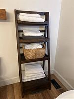 Front view of dark stained wooden ladder shelf with towels and basket on shelves