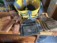 Overview image showing yellow nylon tool bag, multiple brown and black leather tool pouches on wooden table.