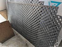 Four large and four small black PVC lattice panels leaning against a wall, stacked partially overlapping, showing diamond lattice pattern.